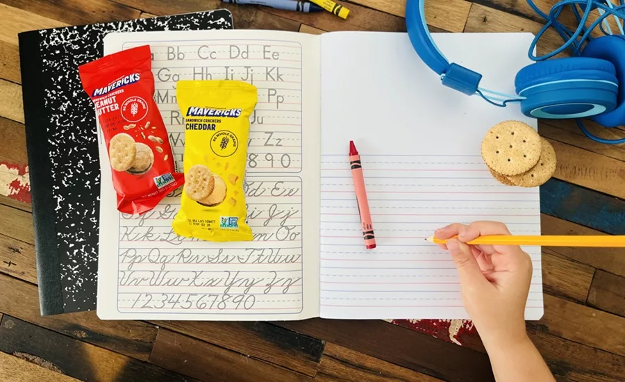 Packages of Mavericks snacks on notebook next to child's hand