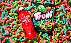 Bottle of Mountain Dew and pack of Trolli gummies on pile of worms