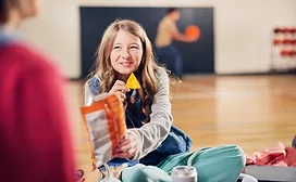 Girl sitting on floor holding out bag of chips