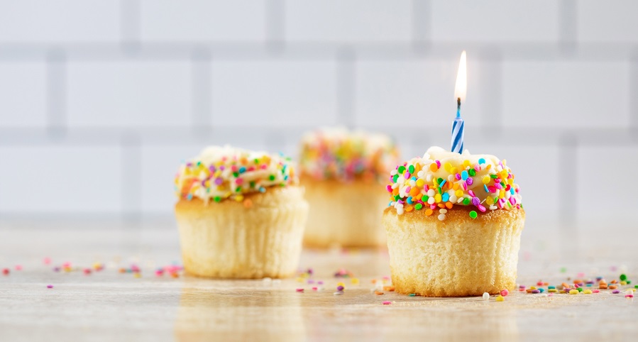 Three cupcakes on a table in front of a subway tile wall