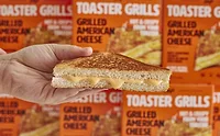 Hand holding grilled cheese in front of Lily's Toaster Grills cartons
