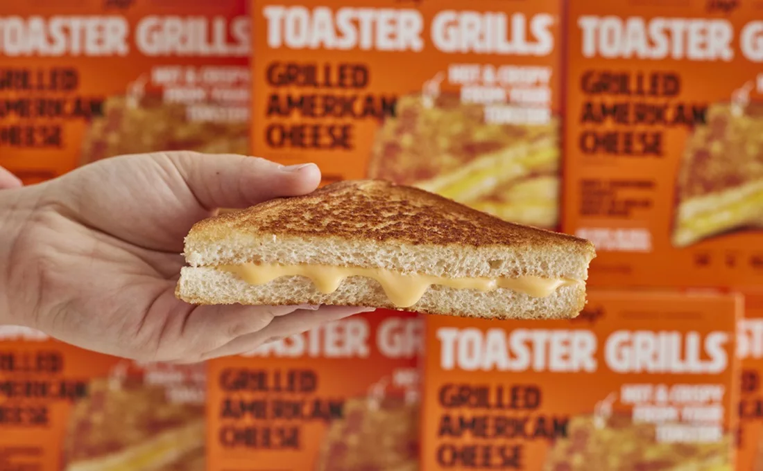 Hand holding grilled cheese in front of Lily's Toaster Grills cartons