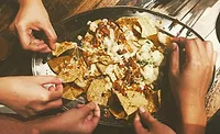 Hands reaching for pieces of loaded nachos from a platter