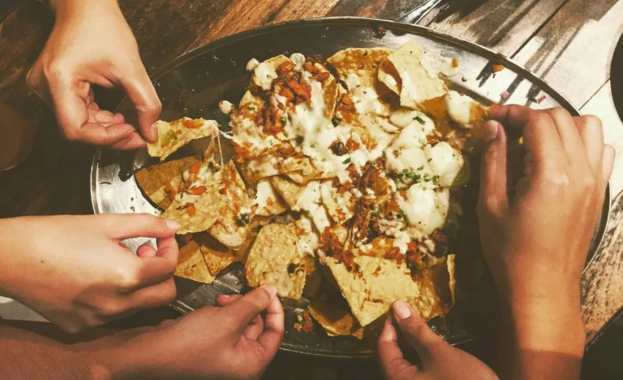 Hands reaching for pieces of loaded nachos from a platter