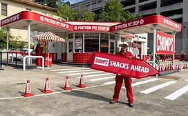 Man holding red Chomps Snacks Ahead sign in front of gas station