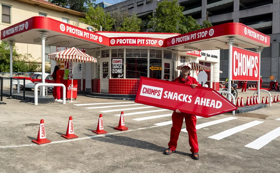 Man holding red Chomps Snacks Ahead sign in front of gas station