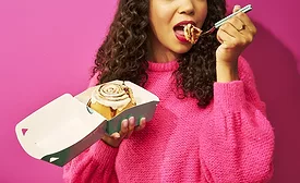 Woman eating Cinnabon roll out of a carton with a fork