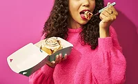 Woman eating Cinnabon roll out of a carton with a fork