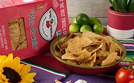 Bowl of tortilla chips on table in front of red bag