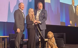 Two men, a woman, and a dog on stage during awards presentation