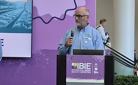 Bald, bearded white man at IBIE podium