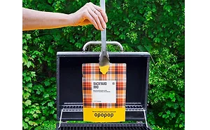 Opopop - bbq.jpg Hand holding tongs with Opopop popcorn bag over grill