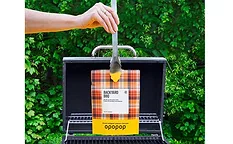 Hand holding tongs with Opopop popcorn bag over grill