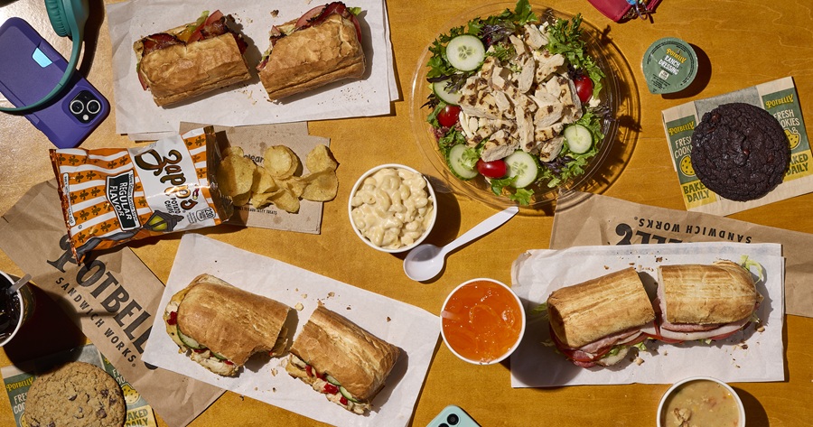 Table loaded with Potbelly sandwiches, cookies, chips, and other food