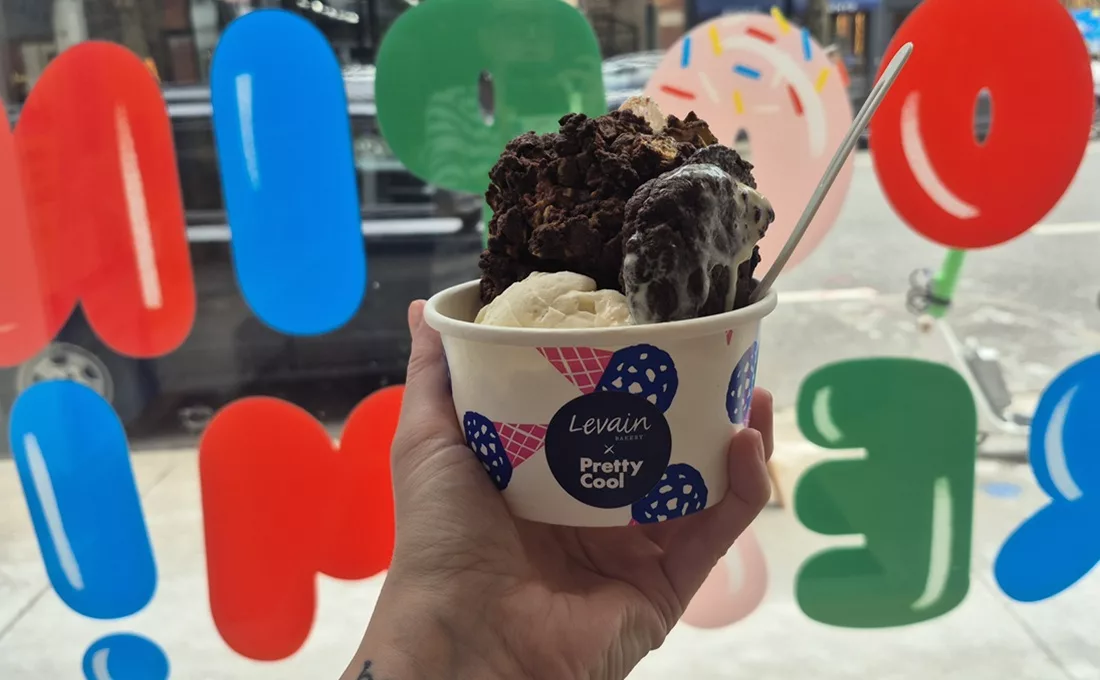 Hand holding ice cream and cookie in a cup in front of a colorful window