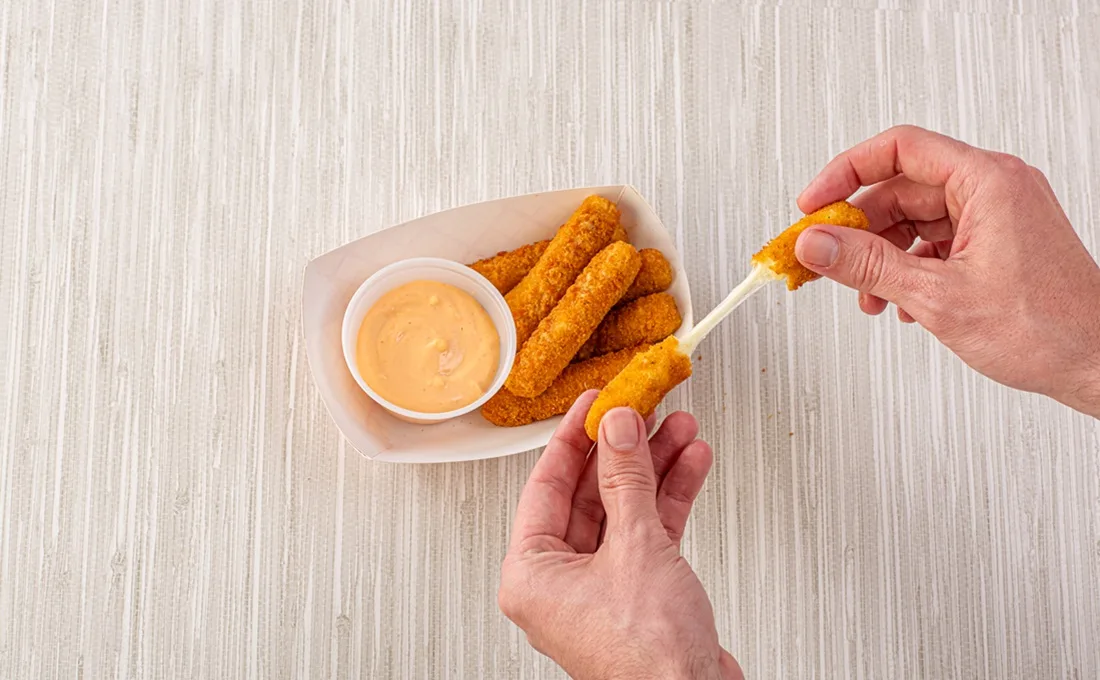 Hands picking up mozzarella sticks over table