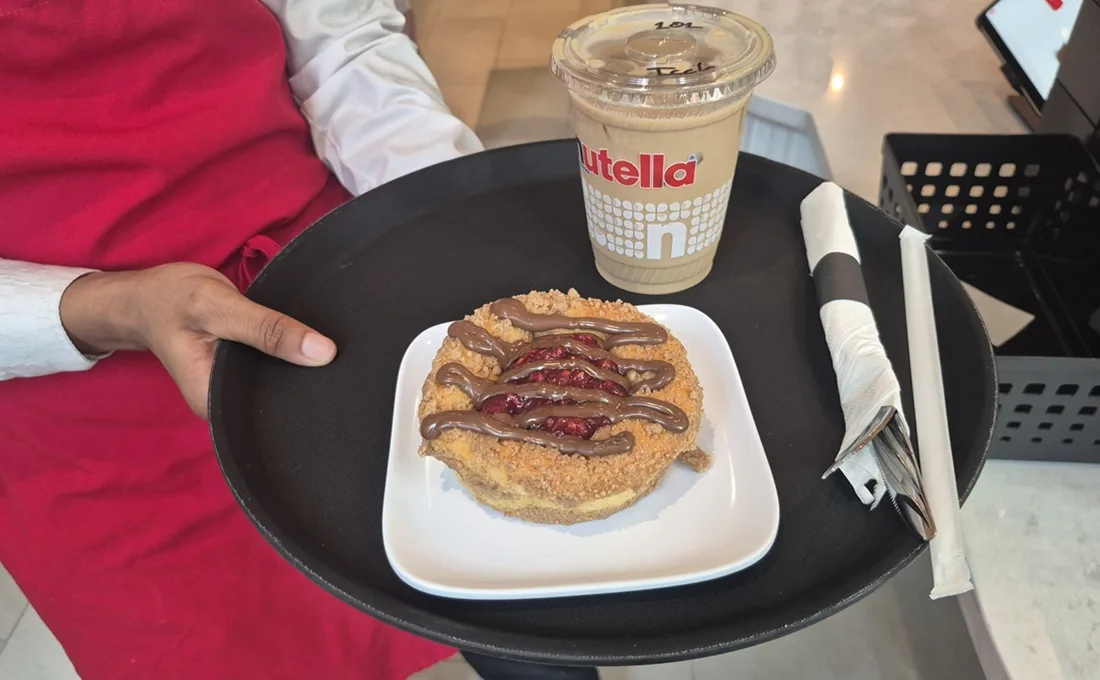 Hand holding Nutella pastry on tray next to cup of iced coffee