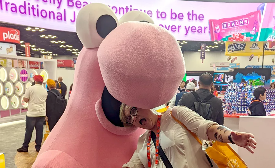 Editor Jenni Spinner on the show floor posing with her head in a Nerds mascot’s mouth