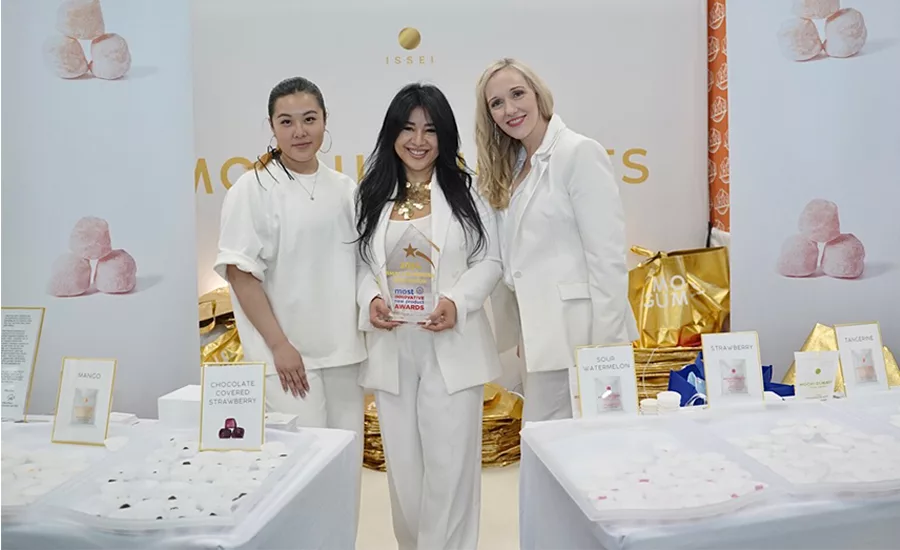 Award winners dressed in white holding an award in their booth behind tables of product