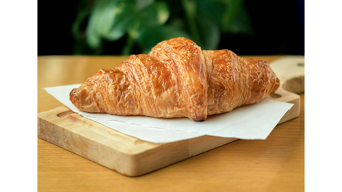Butter croissant on parchment paper atop wood tray