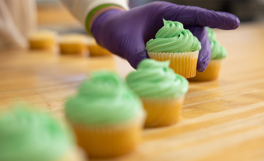 Hand with foodservice glove placing frosted cupcakes in a row