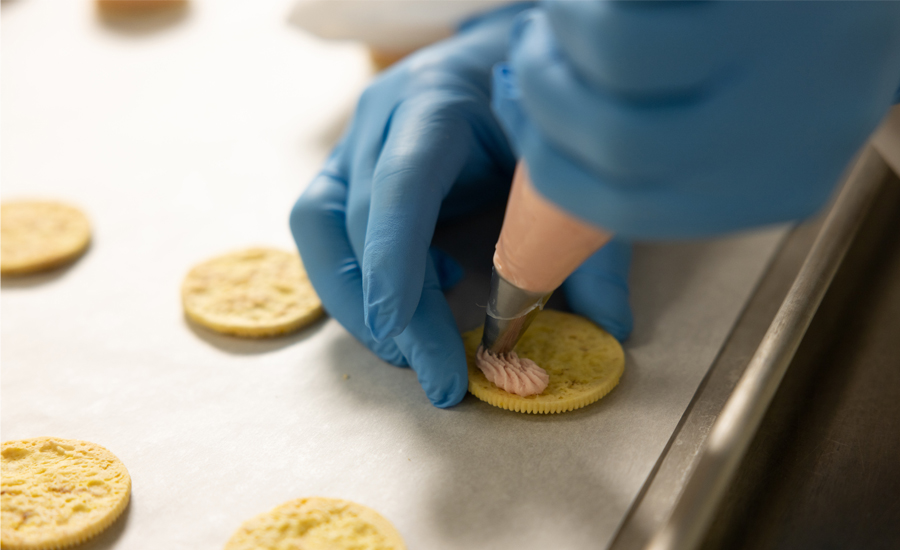 Hand with foodservice glove piping filling onto a cracker