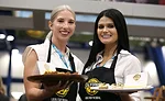 Two women offer samples of bread and cheese on a tray.