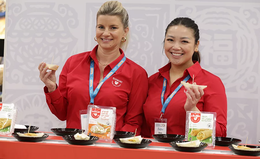 Two women hold up samples of dumplings and spring rolls at IDDBA.