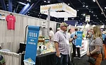 A man and a woman talk in front of a sign that says IDDBA New Exhibitor.