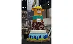 A multi-tiered cake with a cow at the top, at IDDBA 2024.