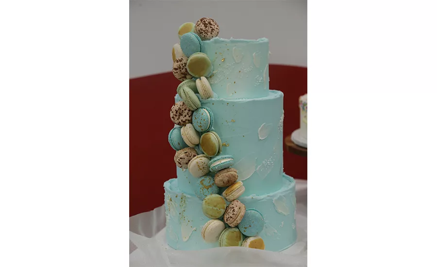 A multi-tiered blue cake with multi-colored macarons stuck to the side.