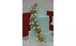 A multi-tiered blue cake with multi-colored macarons stuck to the side.
