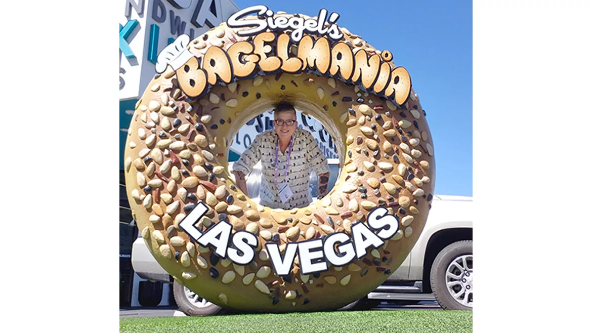 Woman hiding behind giant bagel-shaped Siegel’s Bagelmania sign