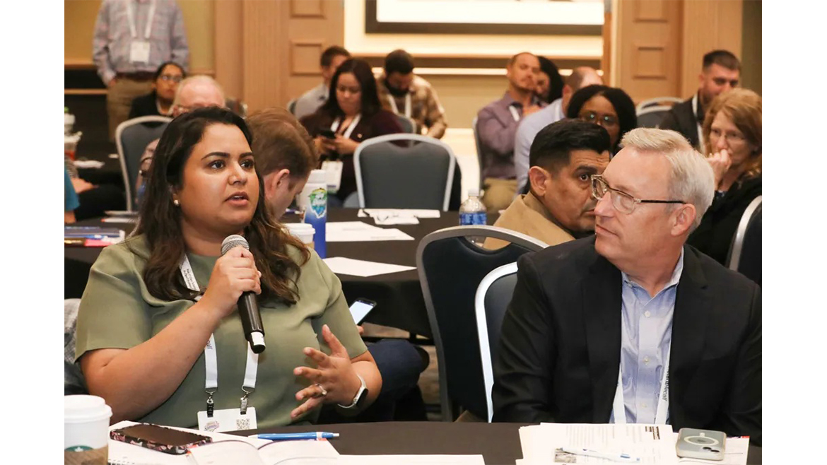 Woman holding a microphone at a table while man looks on