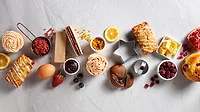 This image displays a collection of ingredients and finished baked goods, including cupcakes, pastries, fresh fruit, jams, and baking tools. This image displays a collection of ingredients and finished baked goods, including cupcakes, pastries, fresh fruit, jams, and baking tools.