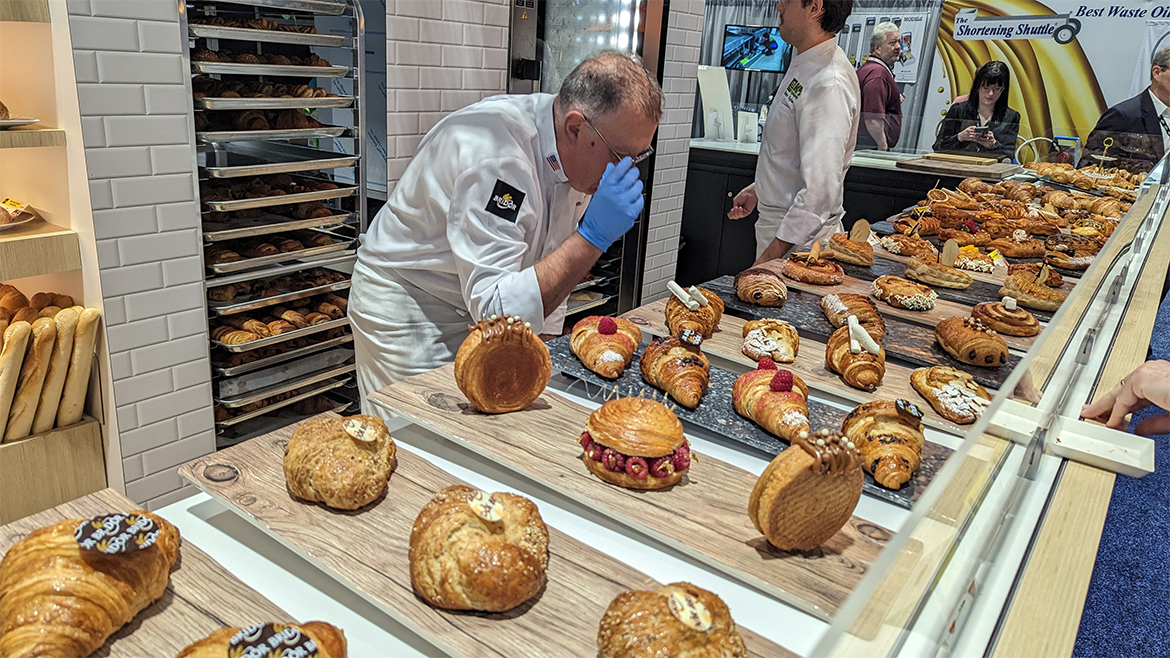a moment of culinary creation in a bakery, likely featuring a pastry chef examining or adjusting a display of freshly baked artisan goods.