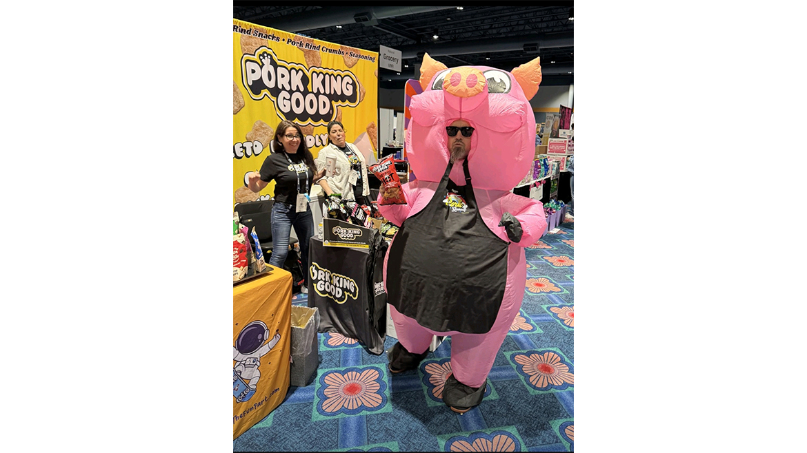 Man in inflatable pig costume in front of Pork King Booth, with two women in the background