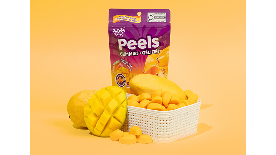 A yellow and purple bag of mango peelable gummies with mangoes in front in a white basket.