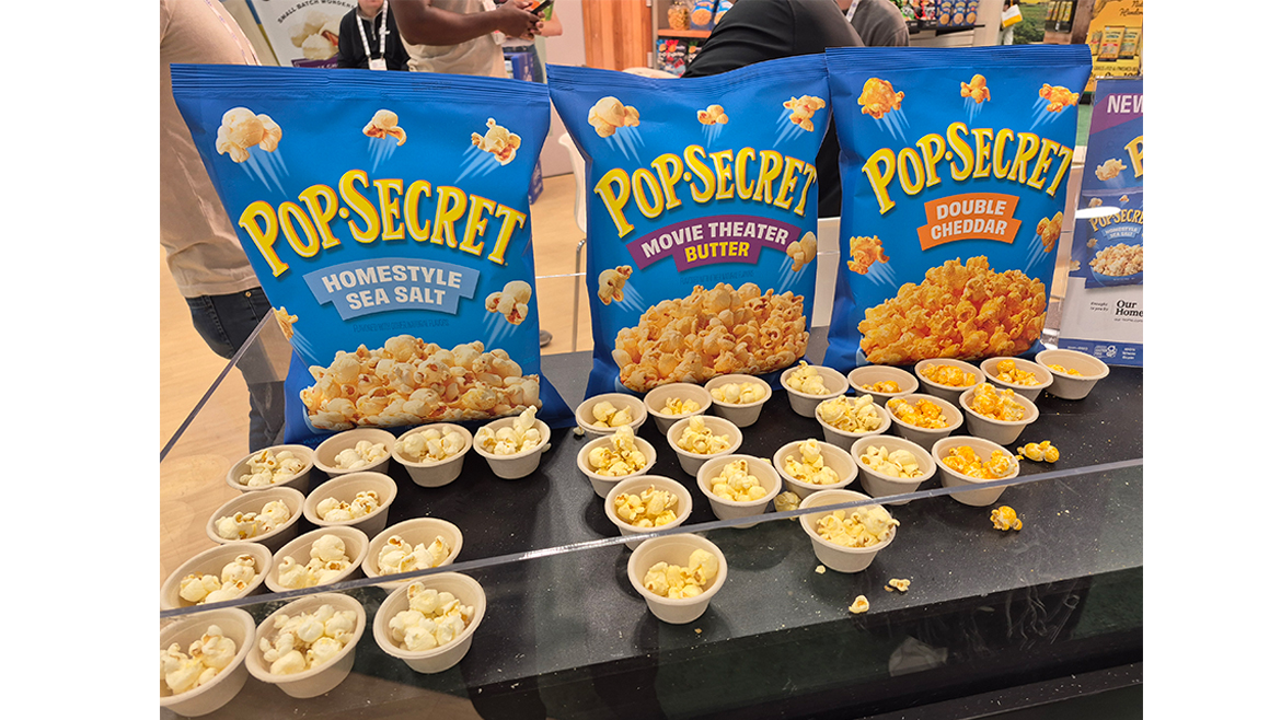 Samples of PopSecret popcorn in blue bags, at the 2025 Sweets & Snacks Expo.