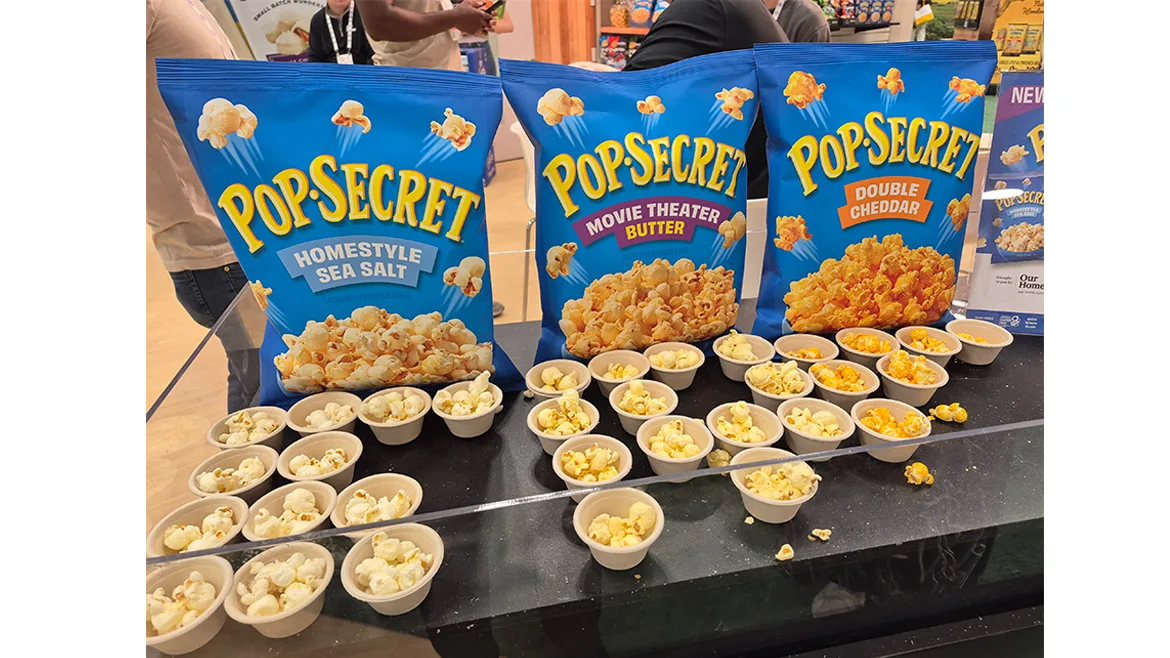 Samples of PopSecret popcorn in blue bags, at the 2025 Sweets & Snacks Expo. Samples of PopSecret popcorn in blue bags, at the 2025 Sweets & Snacks Expo.