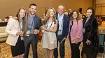 This image shows a group of people smiling and posing together, likely at a professional conference or networking event. 