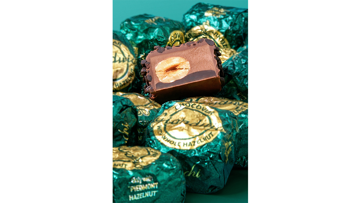 Pile of green-wrapped chocolates and unwrapped truffle on green background