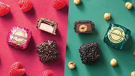 Wrapped and unwrapped chocolate pieces, berries, and nuts on pink and green background