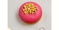 Pink doughnut with yellow sprinkles on white table
