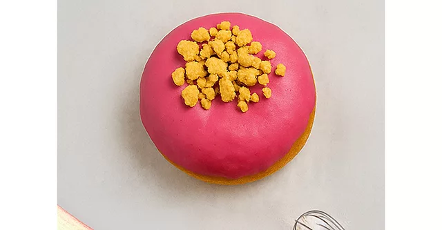 Pink doughnut with yellow sprinkles on white table