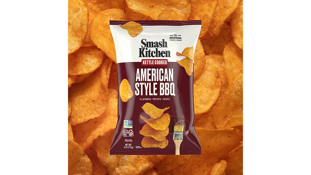 A brown and white bag of Smash Kitchen Kettle Cooked American Style BBQ chips, with chips in the background.