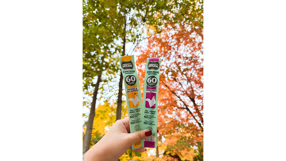 Hand holding two multicolored packs of Mighty Spark meat sticks