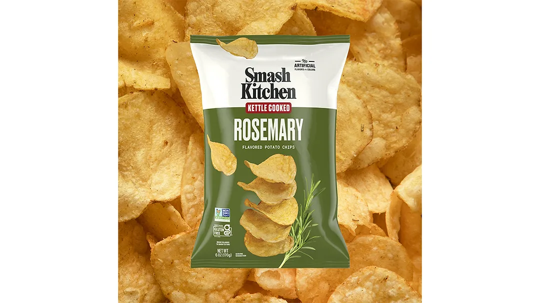 A green and white bag of Smash Kitchen Kettle Cooked Rosemary chips, with chips in the background.