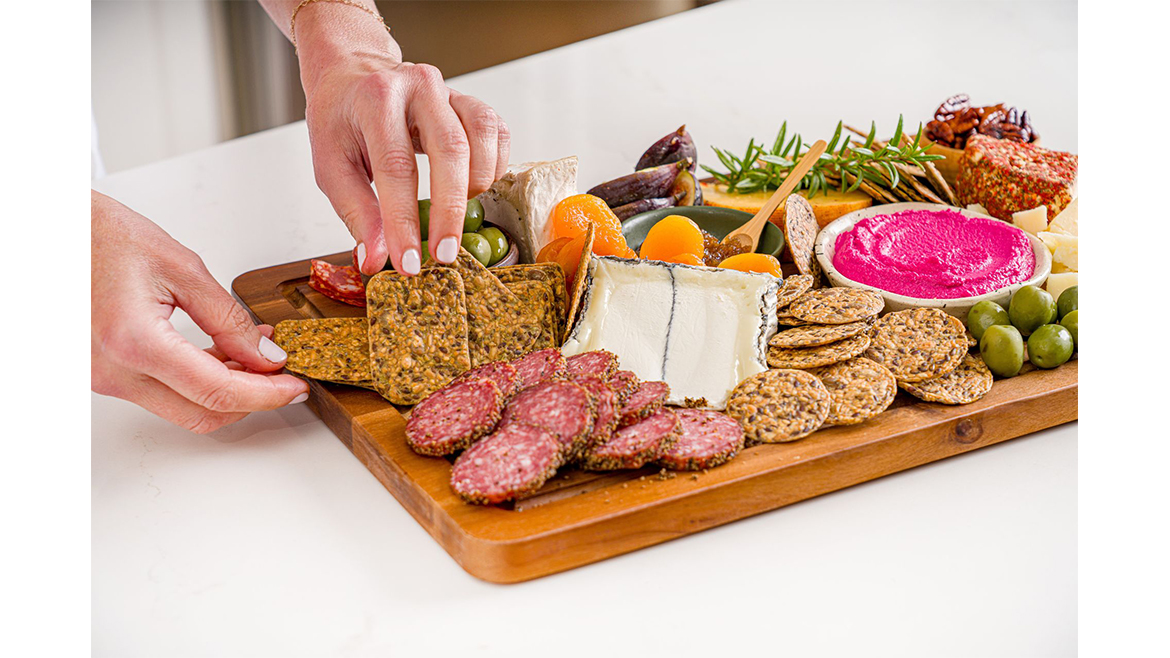 Hand arranging crackers and other items on a charcuterie board