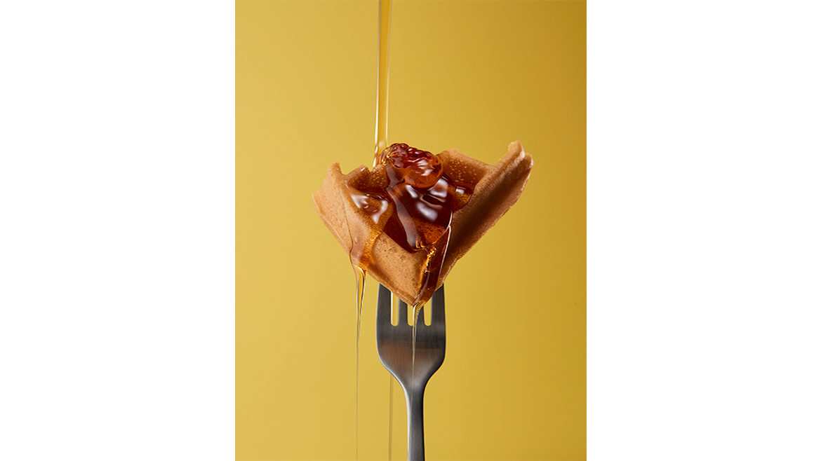 Piece of waffle on fork with syrup drizzle